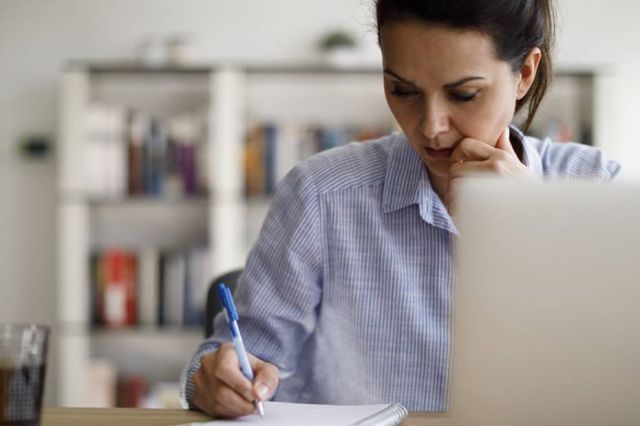 A woman takes notes while reviewing her digital assets on a laptop