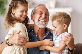 A picture showing a mature man playing his two grandchildren happily.