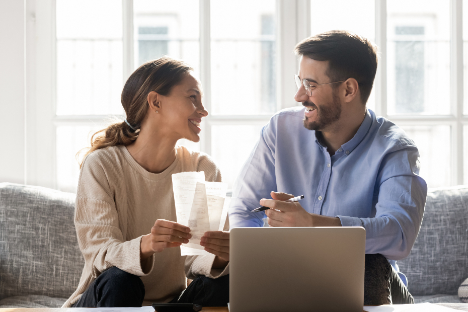 A smiling couple on a couch, working on a budget