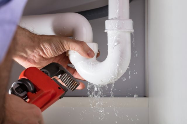 Male Plumber Fixing Dripping Sink Pipe With Adjustable Wrench