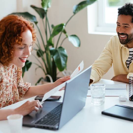 A smiling couple at a table with a laptop and papers