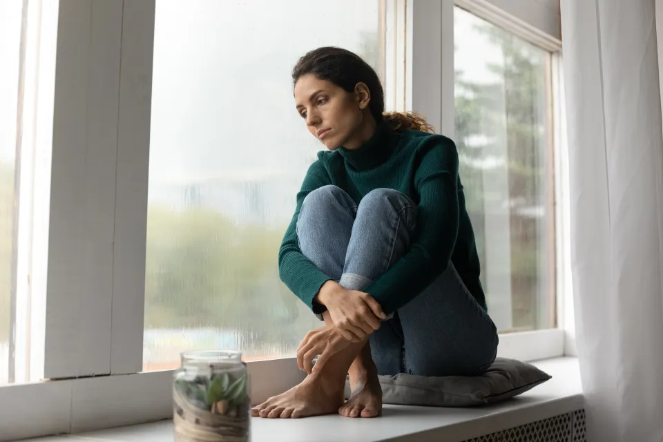 Sad person sitting near a windowsill