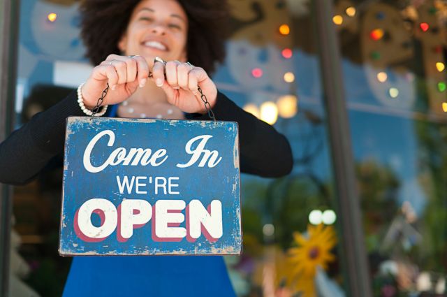 Woman holding vintage open sign up outside of a boutique store front. Photograph taken in Grand Rapids, Michigan.