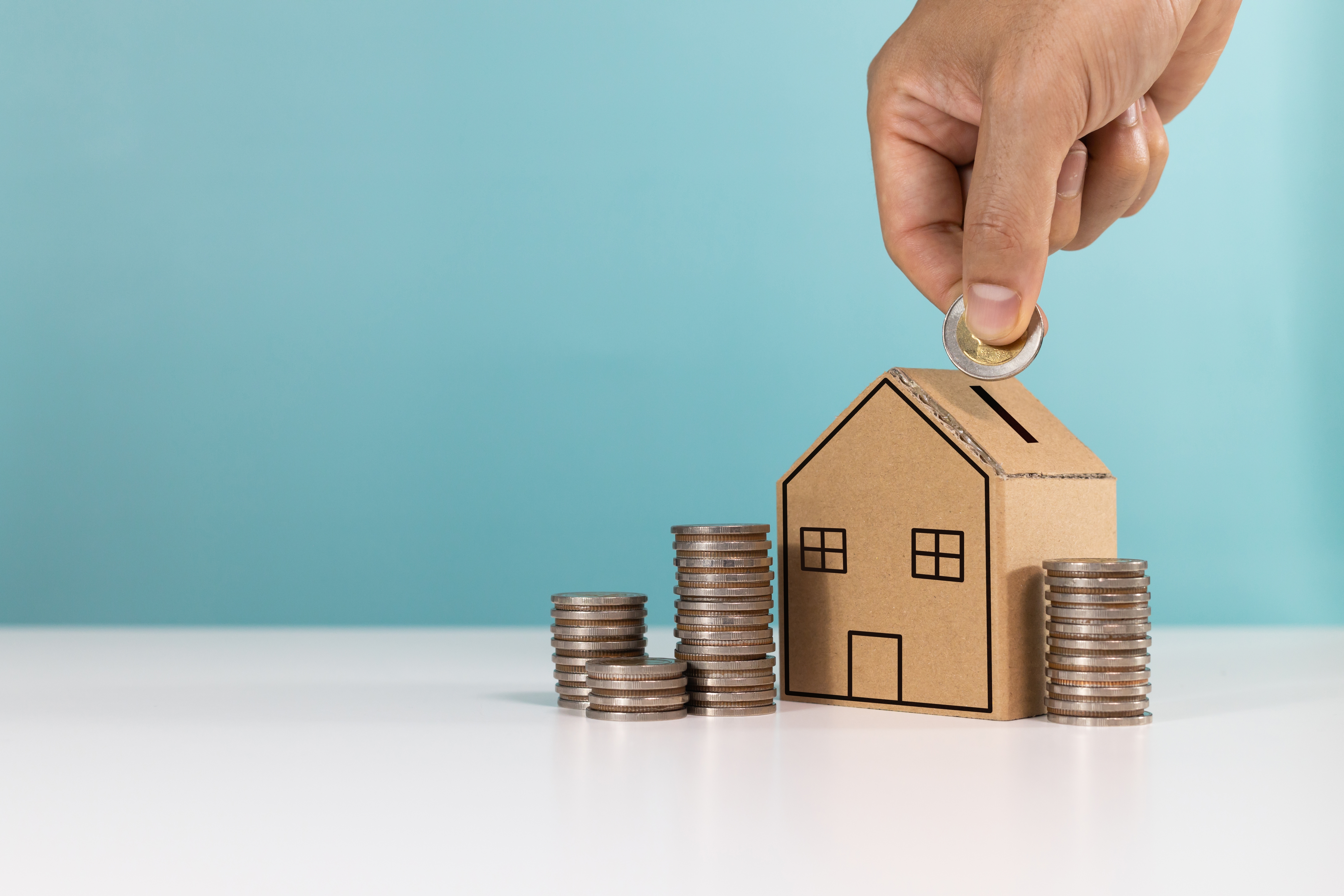 Hand dropping coins into a piggy bank shaped as a house.