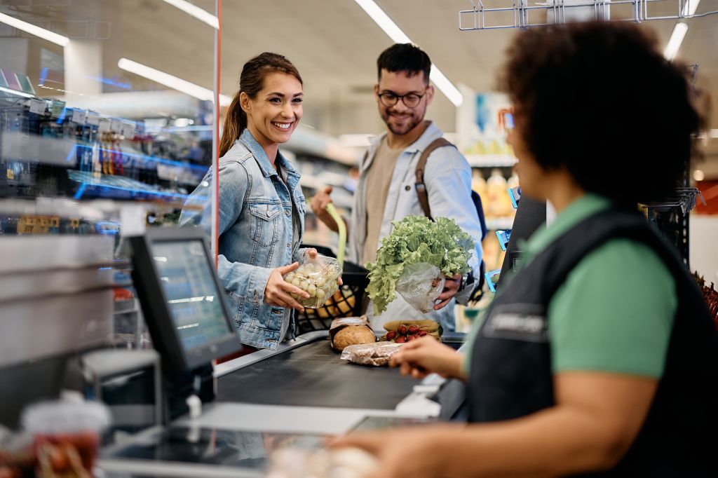 Happy couple talking to cashier while putting groceries on checkout counter in supermarket