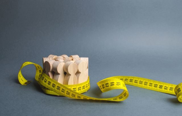 A crowd of wooden figures gripped by measuring tape