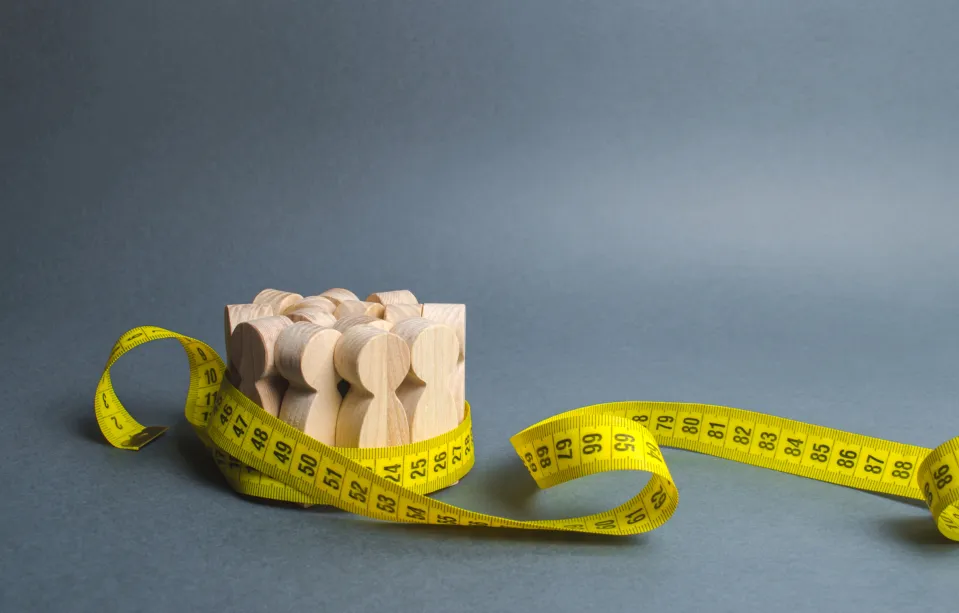 A crowd of wooden figures gripped by measuring tape