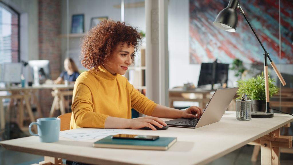 A professional employee sits at her desk looking at her laptop