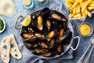 Moules et quartier de citron dans une poêle avec des frites à côté et deux tranches de baguette.