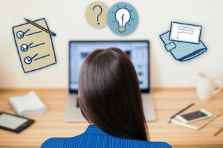 Assise à son bureau, une femme regarde son ordinateur.