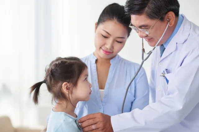 Jeune fille asiatique accompagnée de sa mère regardant le pédiatre qui l'examine.