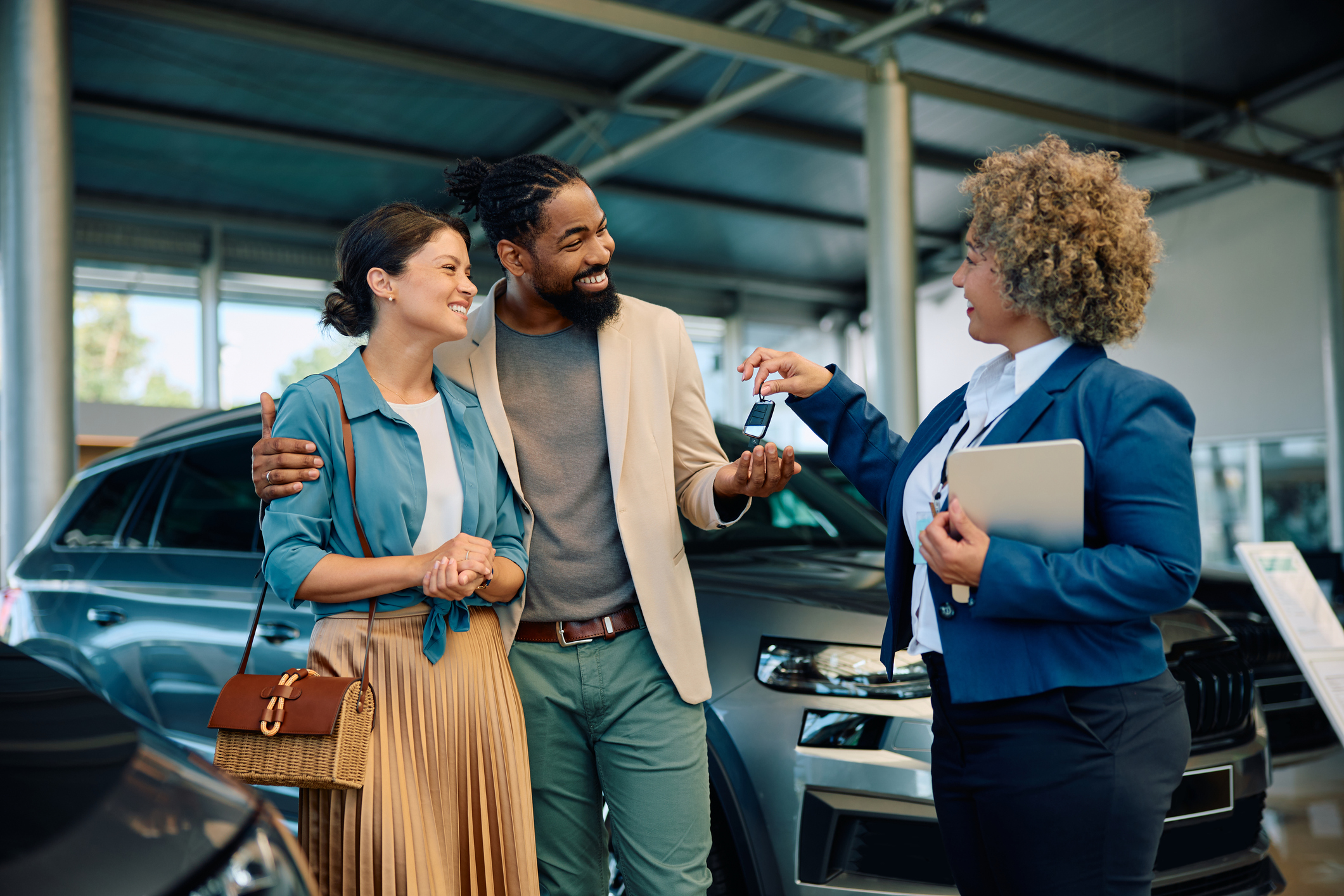 Joyeux couple multiracial recevant les clés de leur nouvelle voiture de la part d'une vendeuse dans la salle d'exposition.