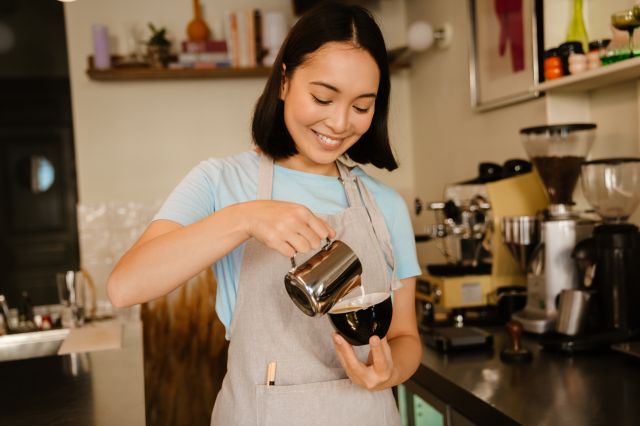 Jeune étudiant international travaillant comme barista, portant un tablier travaillant dans un café