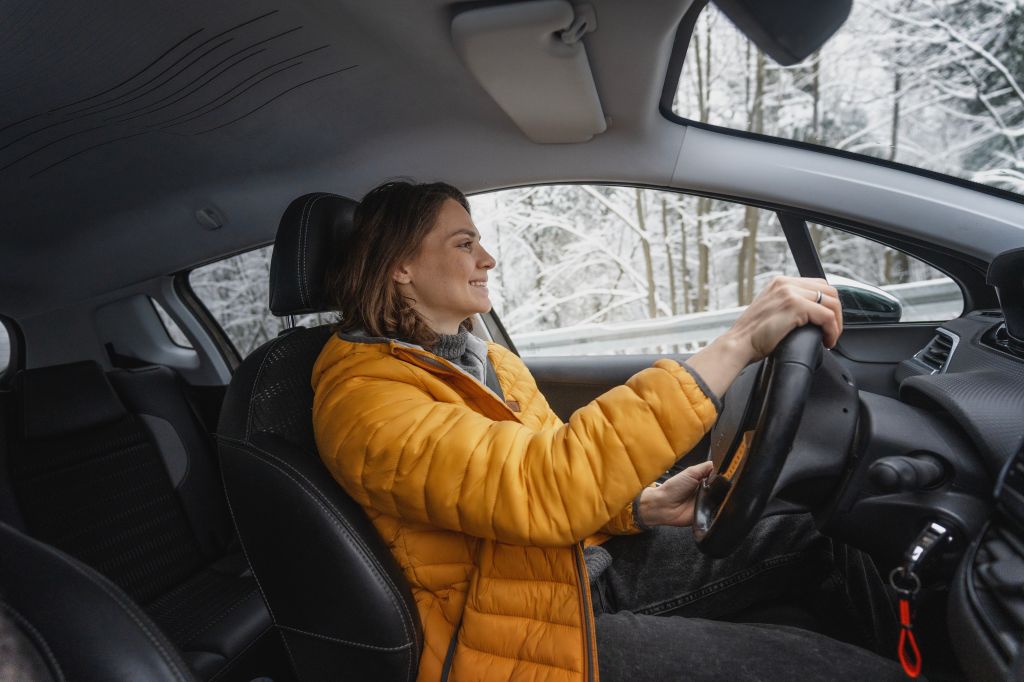 Jeune femme heureuse au volant de sa voiture en hiver