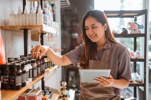 Une employée restoque les étalages dans le magasin où elle travailleImage ALT Text: Une nouvelle employée vérifiant le nombre de produits sur les étagères.